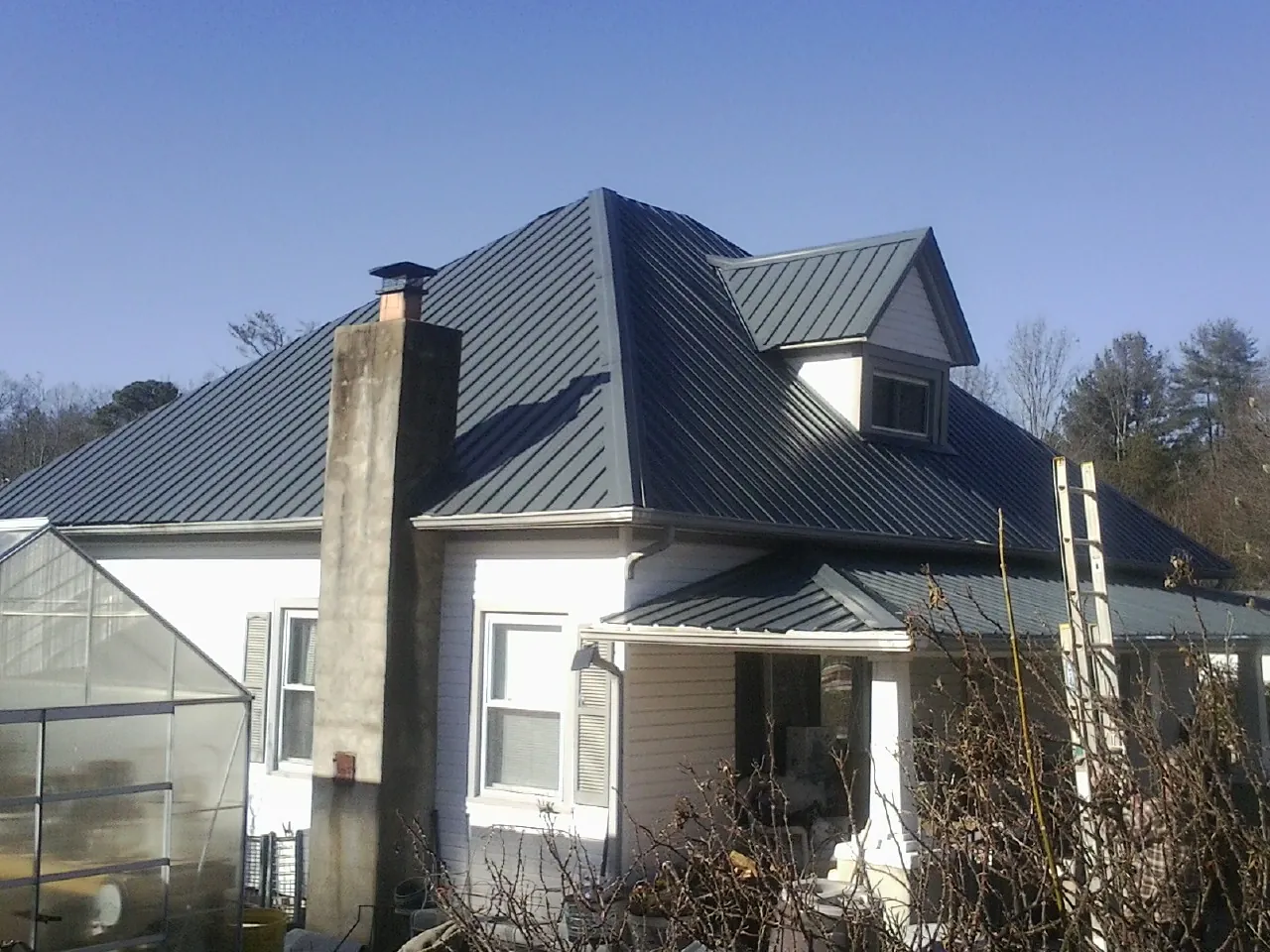 Dark blue standing seam metal roof on a white farmhouse with dormer — Slate & Tile Roof Repair by Roofing Brothers in Woodruff