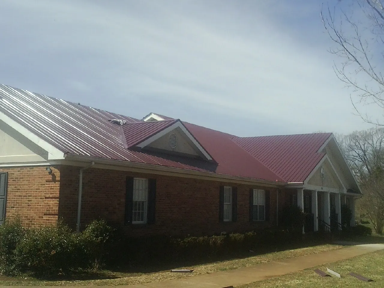 Red metal roof with gabled entries on a long brick building, from a Hail Damage Roof Repair job in Woodruff
