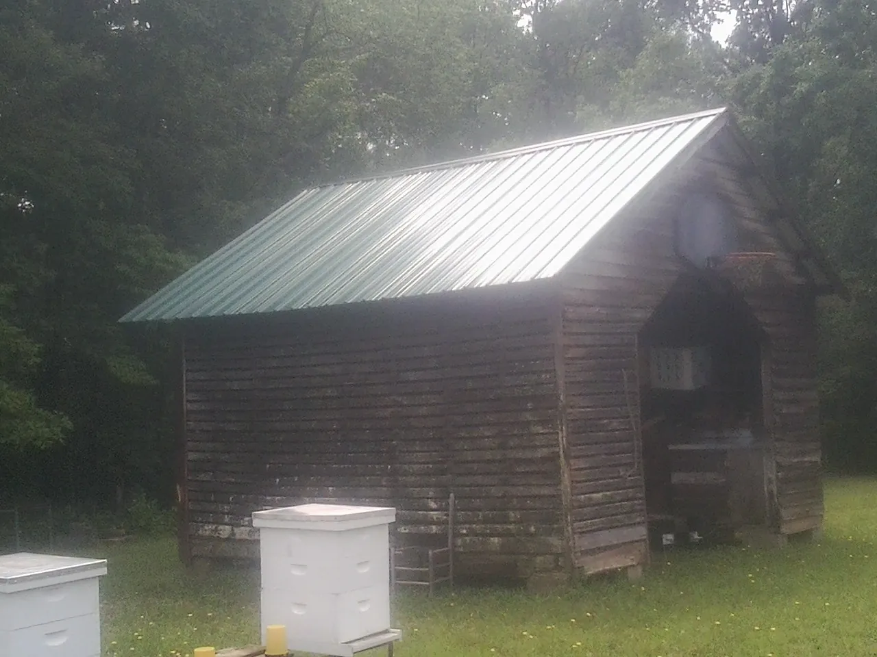 Green metal roof on a weathered barn beside stacked beehives in Woodruff