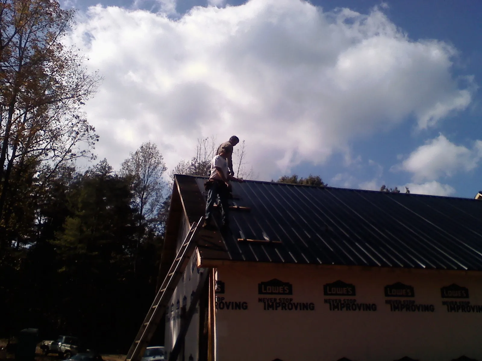 Roofer fastening dark metal panels high against a cloudy sky, from a Roof Inspection job in Woodruff