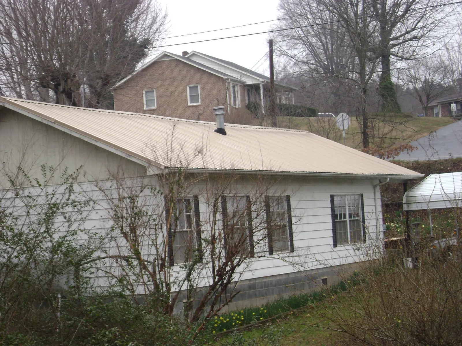 Tan metal roof on a white sided house set into a hillside — Commercial Roofing by Roofing Brothers in Woodruff
